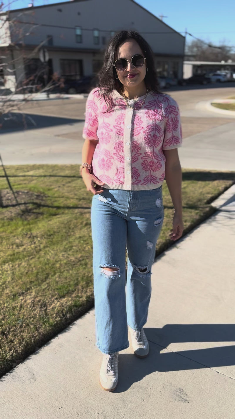Woman wearing a pink floral blouse and blue jeans outside.