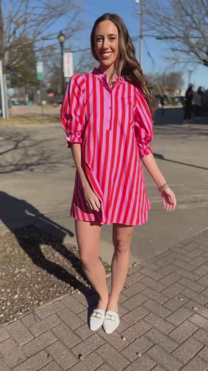 Woman in a pink and red striped dress standing outside.