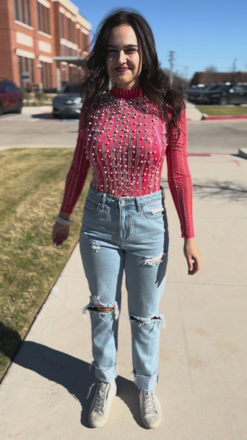 Woman wearing a red patterned top and light blue jeans outdoors.