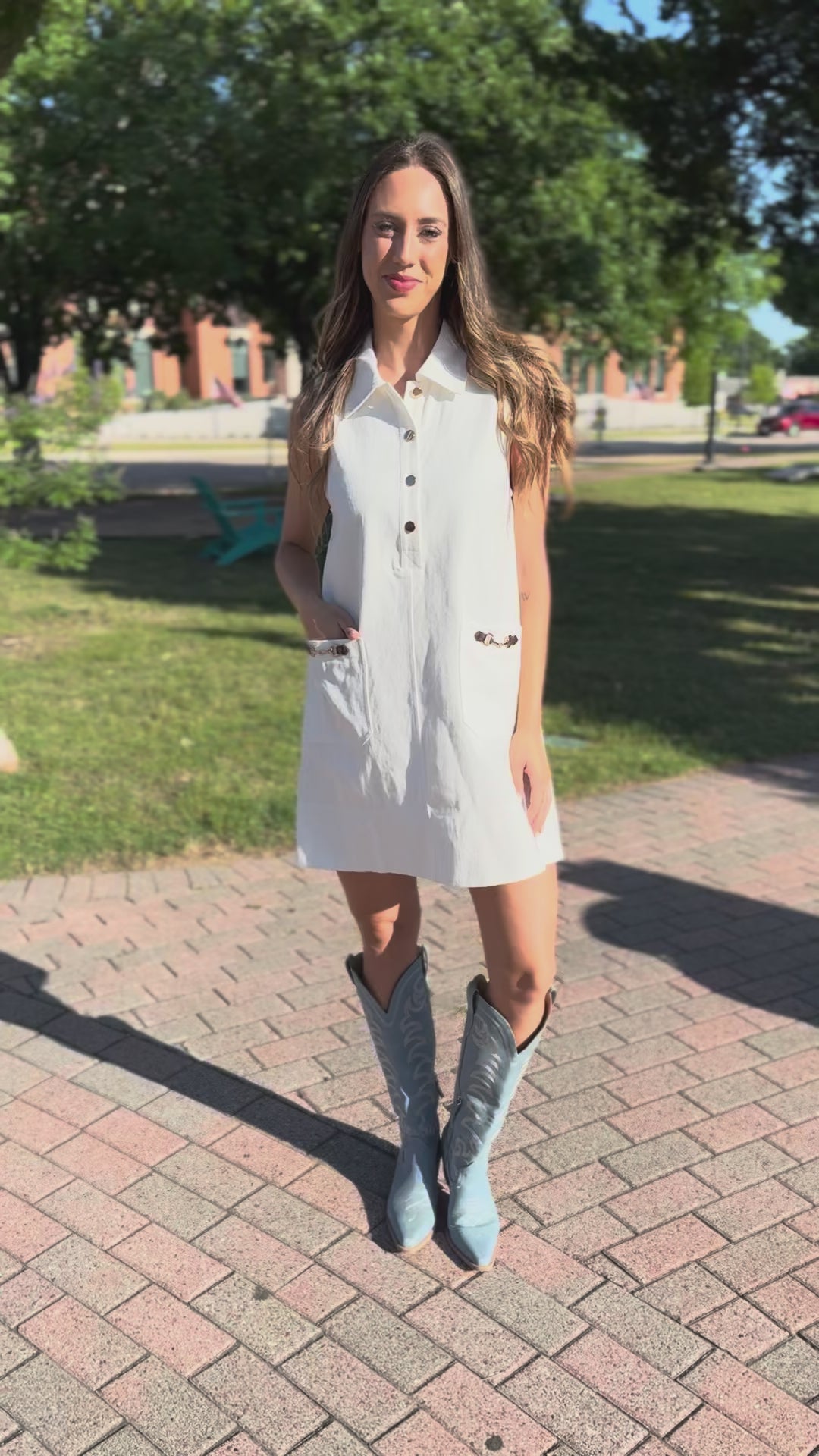 Woman in a white dress and blue cowboy boots standing on a sidewalk.