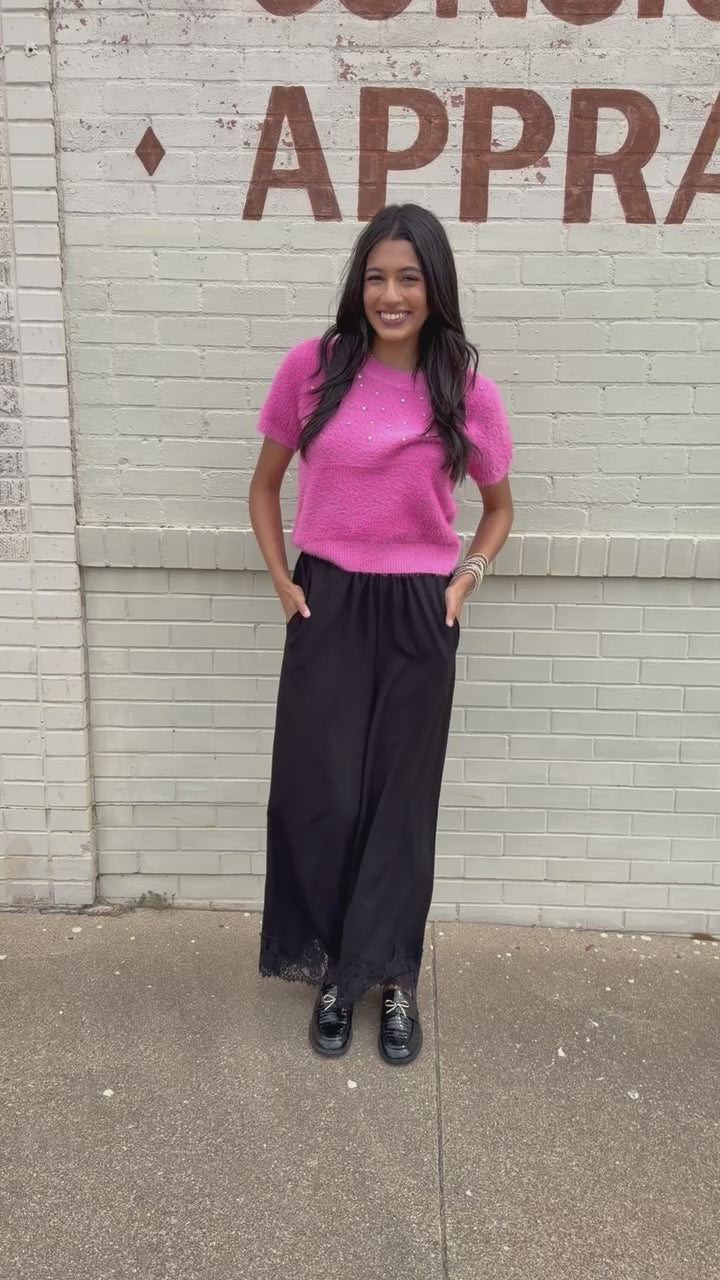 Brunette model wearing the Liora Pearl Knit Top –  Flamingo - and the Ellison pants in black with the toulouse flats on standing outside. Southern House Clothing