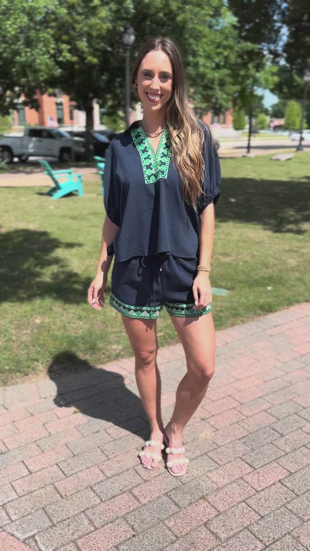 Woman wearing a navy blue top and shorts with green embroidery, standing outdoors