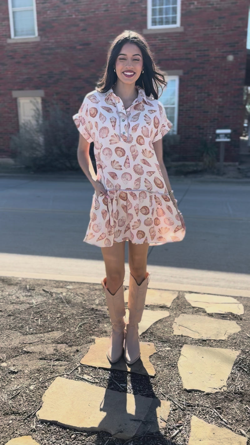 Woman wearing a floral dress and beige boots standing outside.
