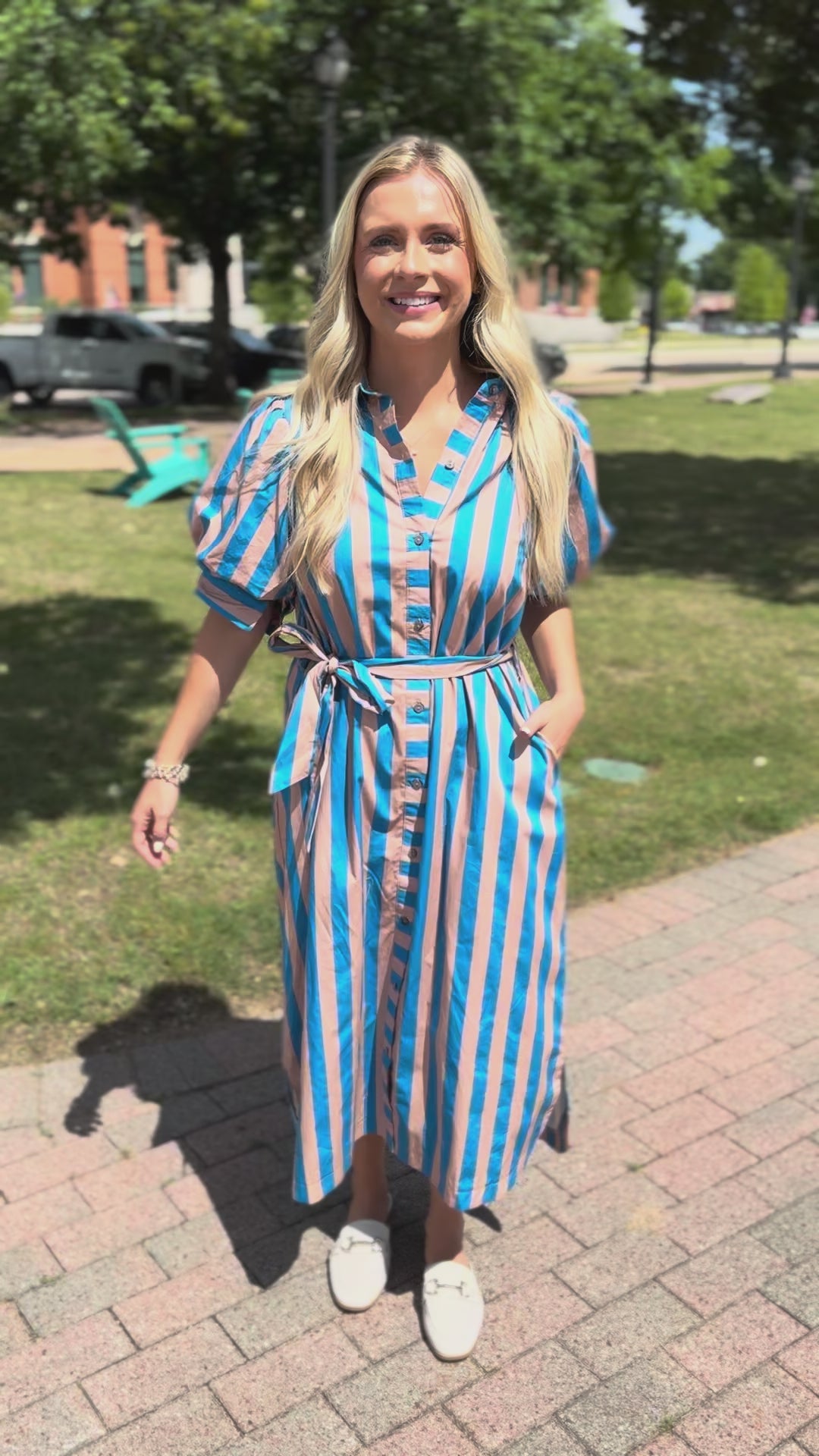 Blonde model wearing a blue and brown striped maxi dress, standing outside.