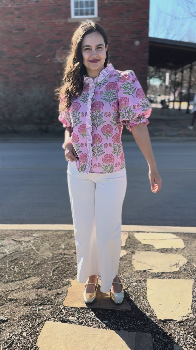 Woman wearing a pink floral blouse and white pants outdoors.