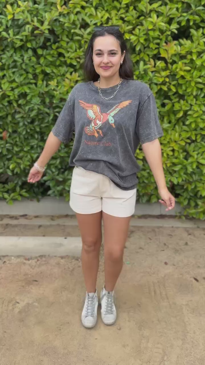 Woman wearing a graphic t-shirt with an eagle design and 'Nature Club' text, standing outside.