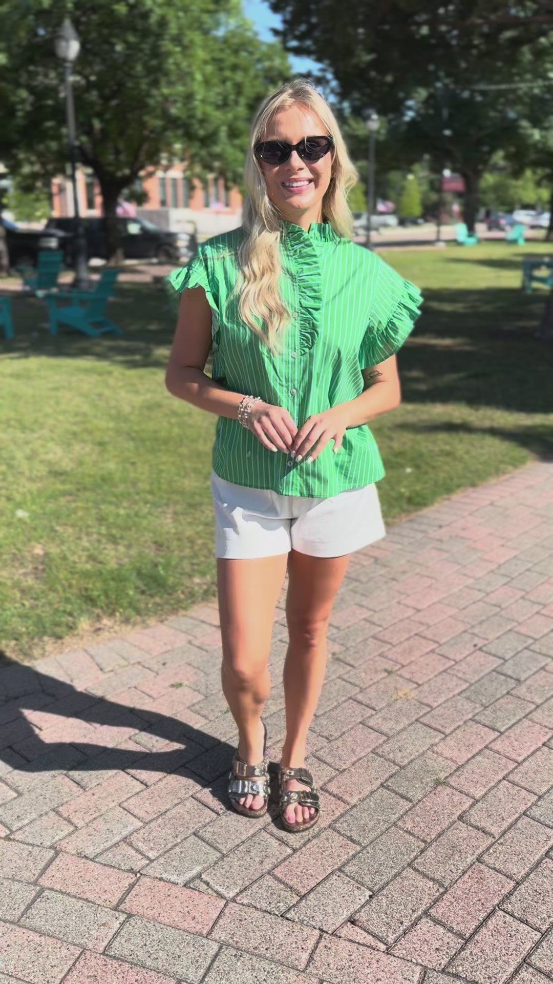 Woman wearing a green and white striped shirt and white shorts standing outdoors.