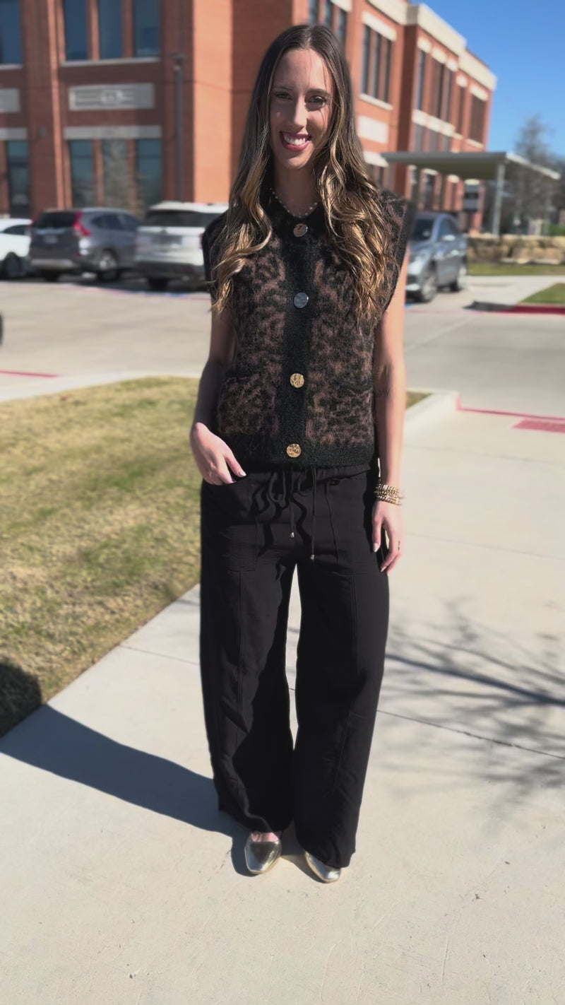 Woman wearing a leopard print cardigan with gold buttons on a city street.