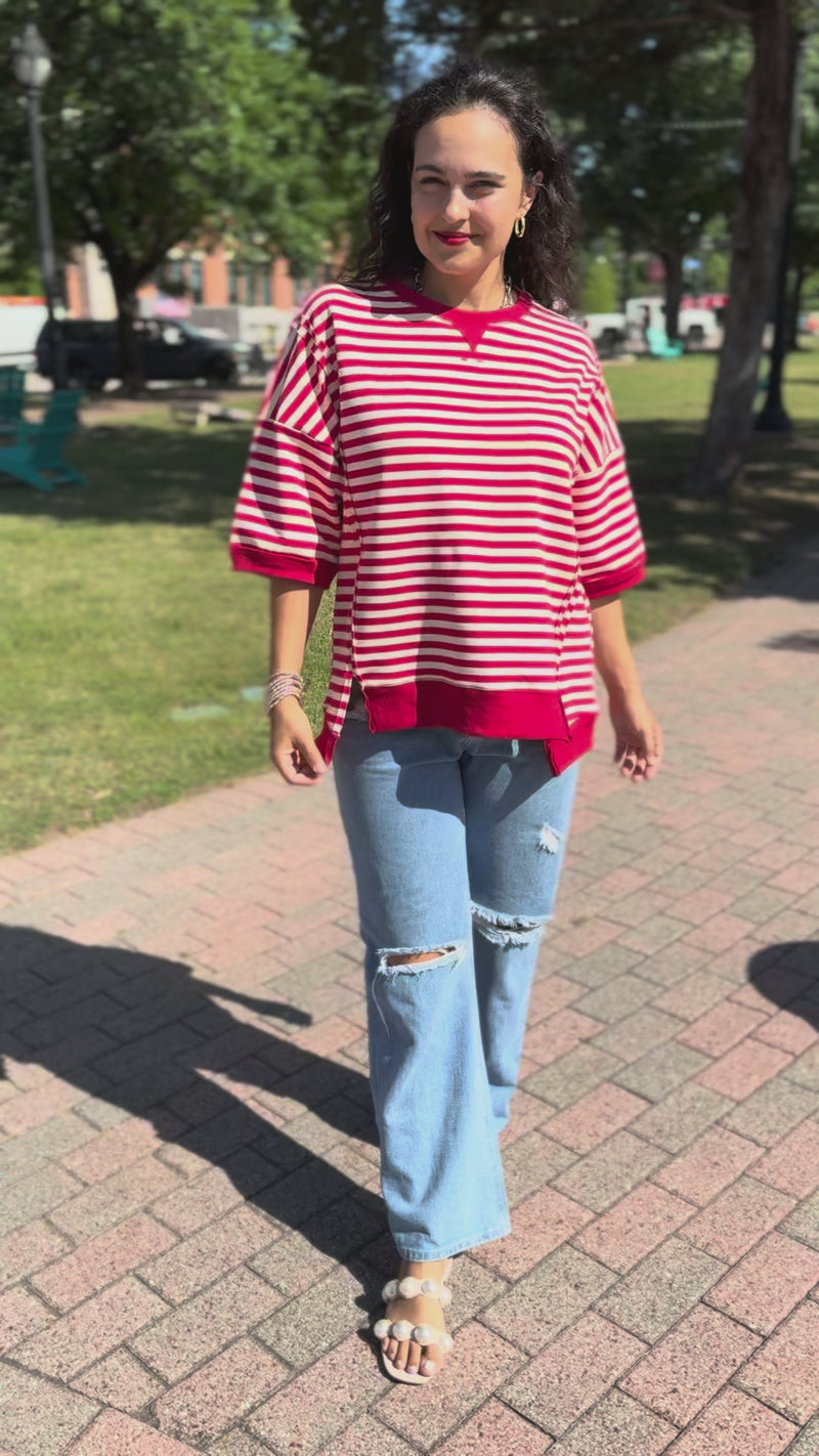 Woman wearing a red and white striped shirt and ripped jeans on a city street.