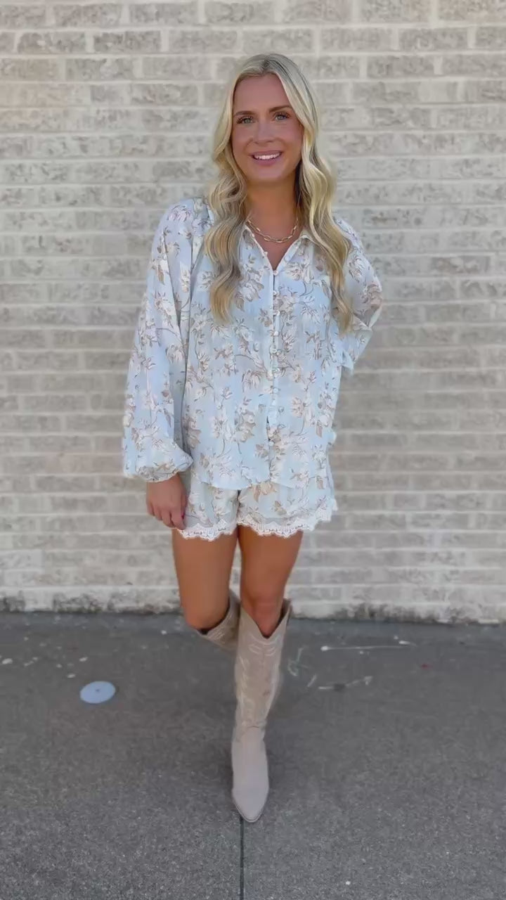 Blonde model standing outside wearing a blue set with lace trim, and tan cowboy boots.