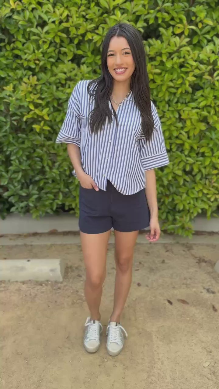 Woman wearing a striped shirt and navy shorts outdoors.