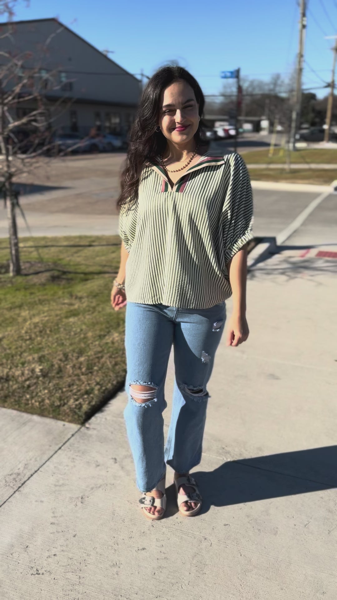 Woman wearing a striped shirt and jeans with sunglasses outside.