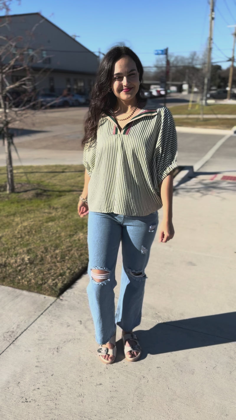 Woman wearing a striped shirt and jeans with sunglasses outside.