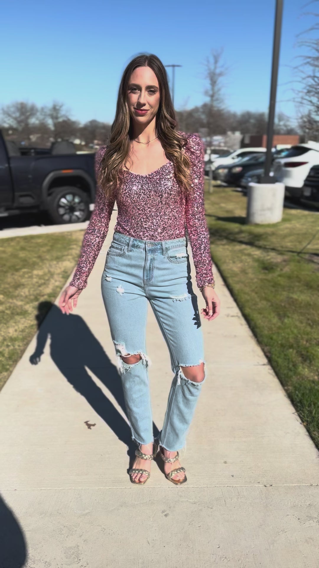 Woman wearing a pink sequin top and blue jeans standing outside.
