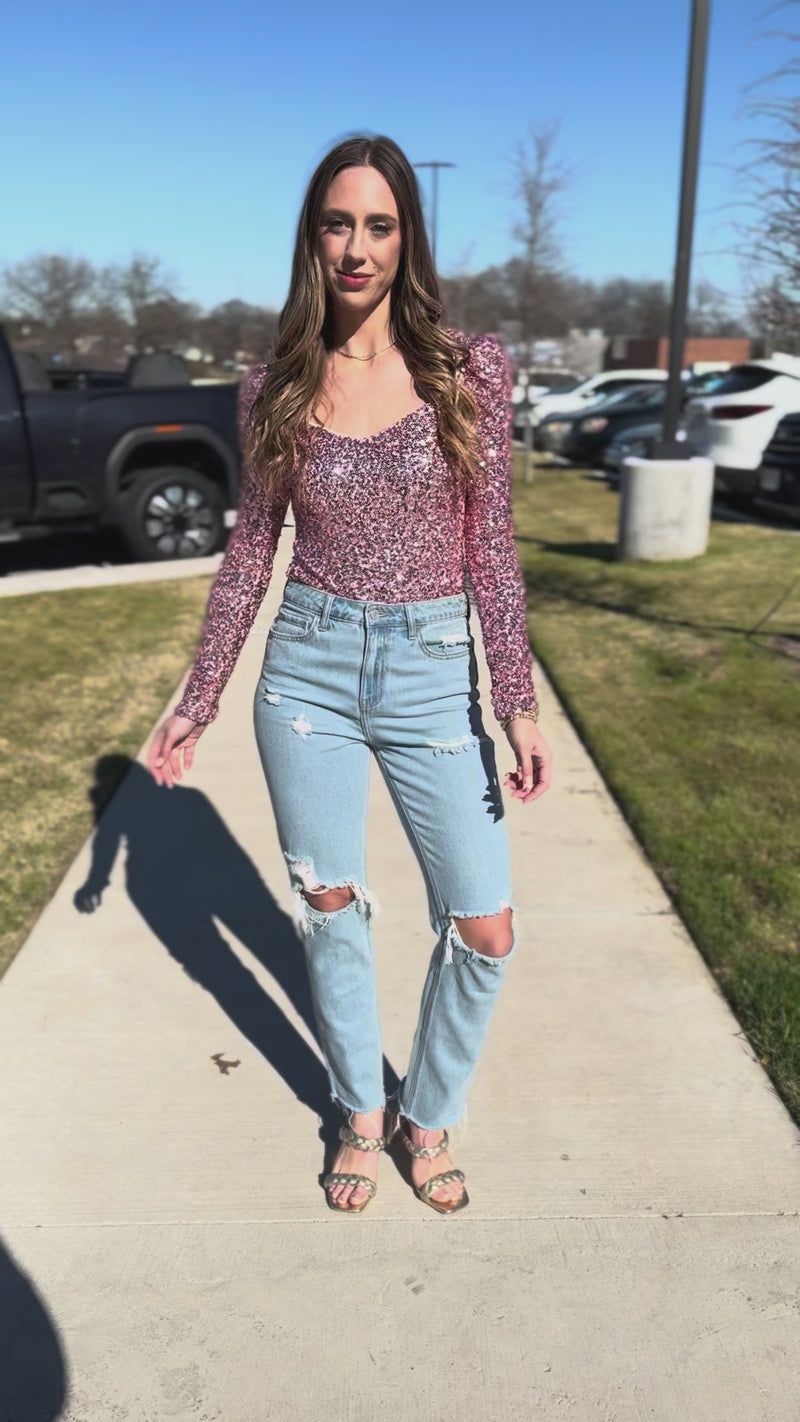 Woman wearing a pink sequin top and blue jeans standing outside.