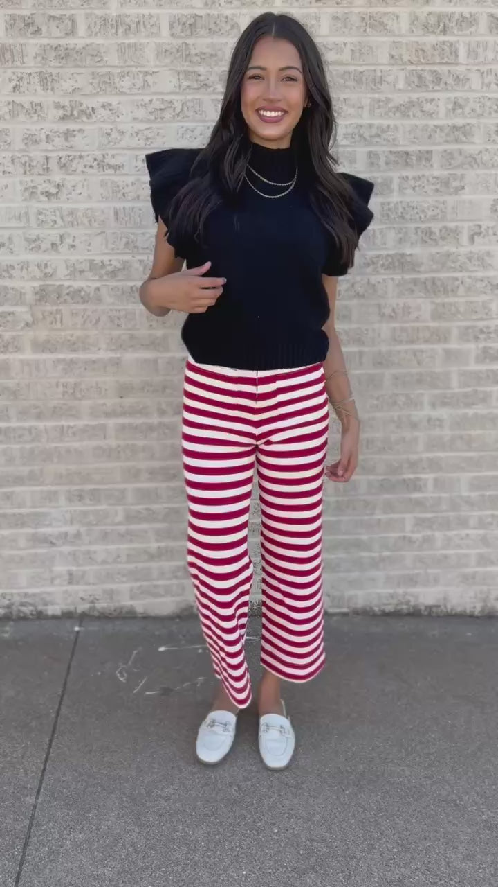 Model wearing a lightweight black sweater with red and white striped pants standing outdoors.