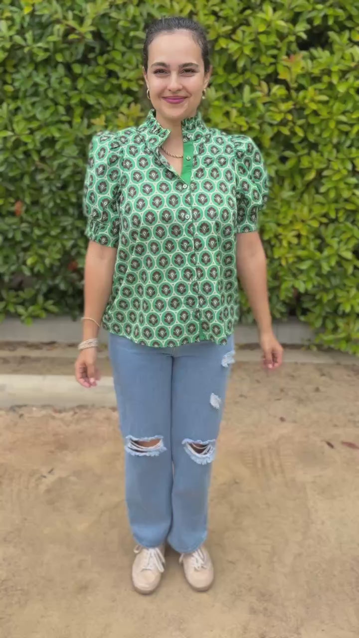 Woman wearing a green patterned shirt and sunglasses, standing outside.