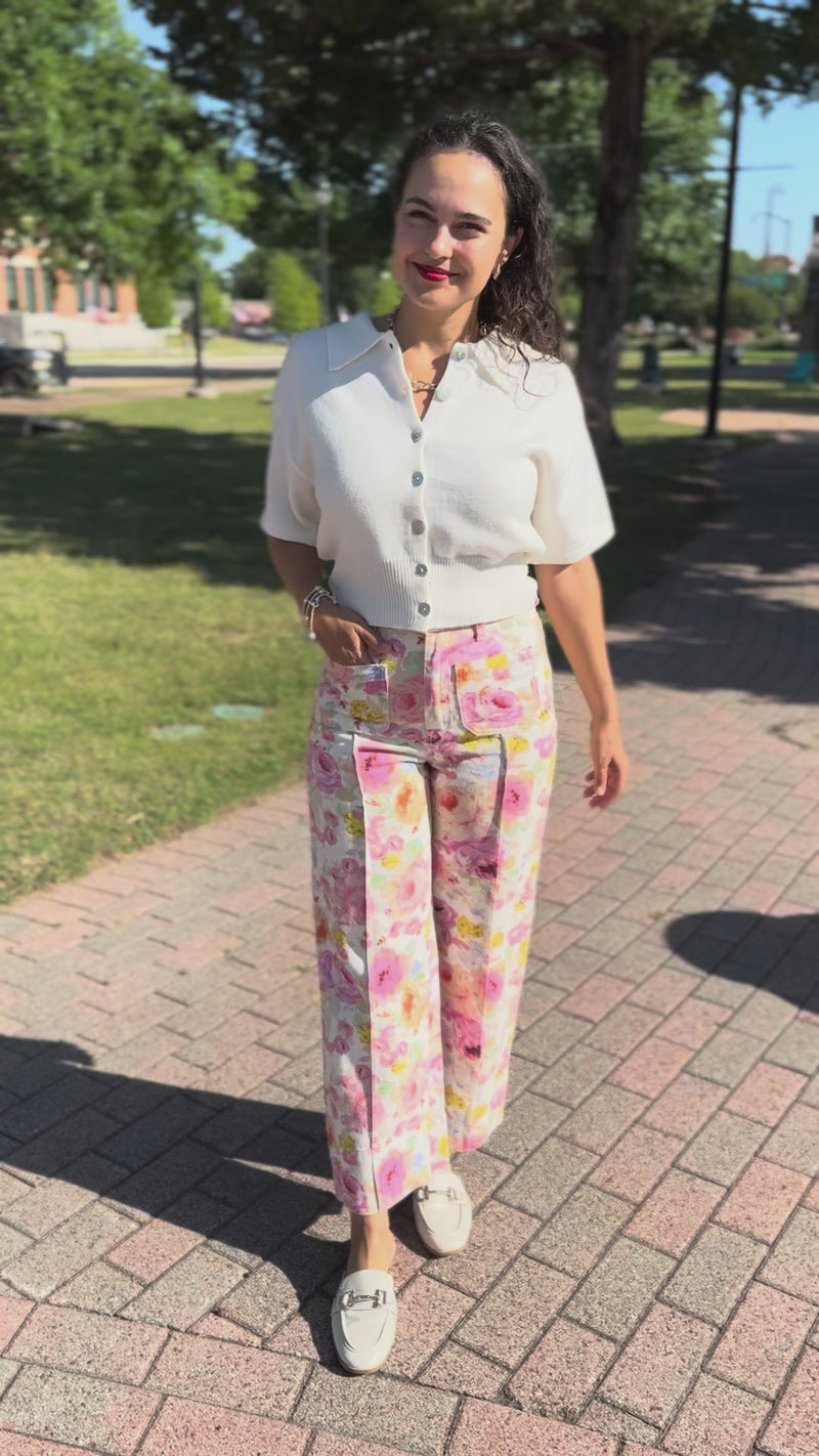 Brunette model standing outside wearing a off white cardigan and floral pattern denim pants.
