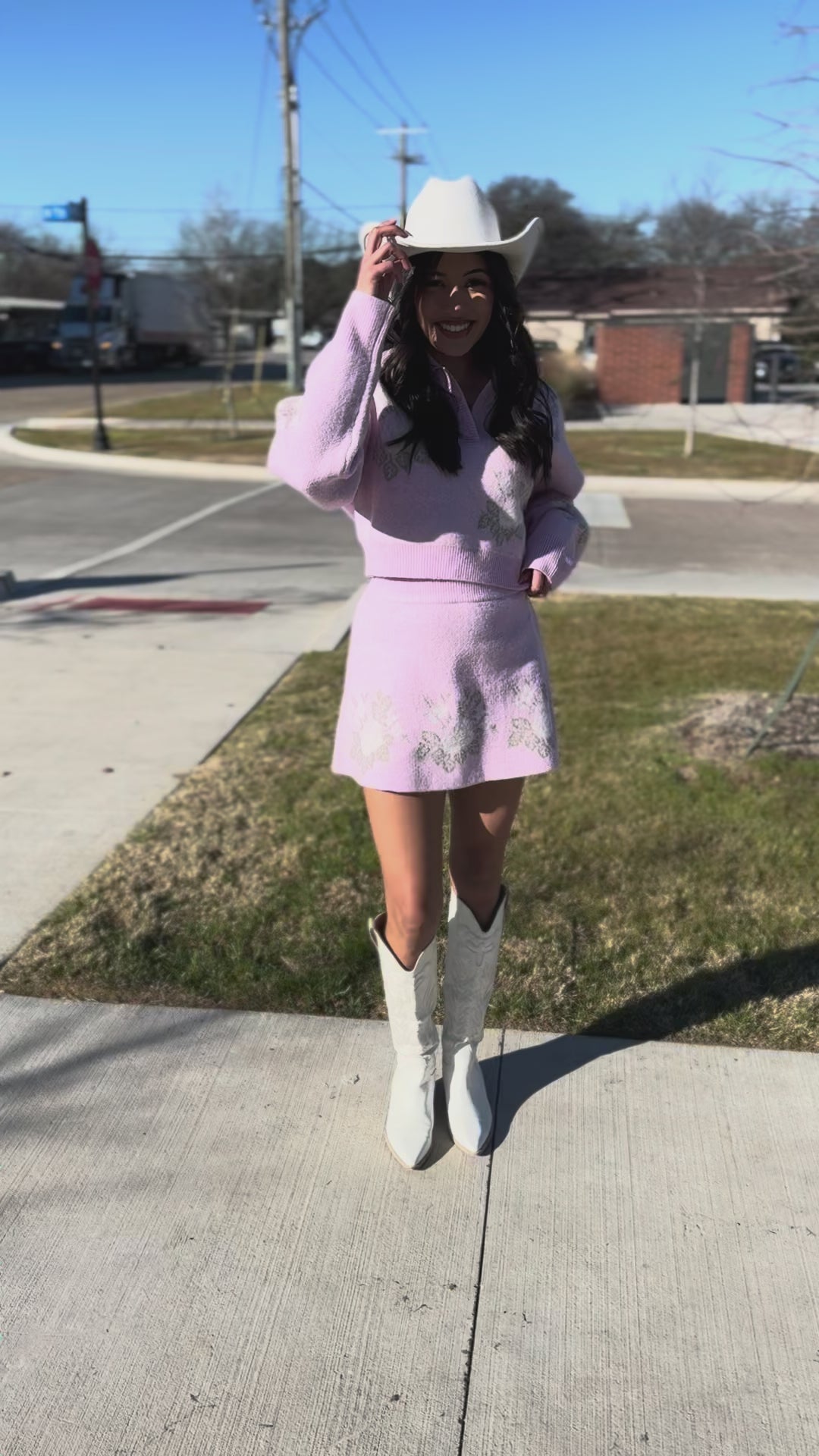 Woman wearing a pink embroidered dress and white cowboy hat outside.