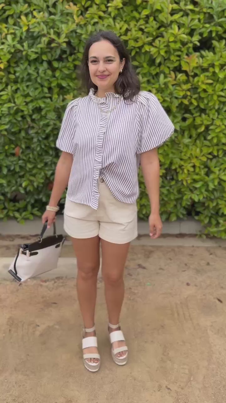 woman with a handbag, wearing a striped shirt and shorts outside.