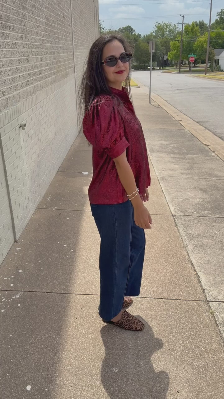 Model wearing the Bellmont Satin Puff Sleeve Blouse in Burgundy with dark-wash wide-leg jeans called the Langley, leopard-print flats called the Atlus, and silver jewelry for a chic casual outfit. Southern House Clothing