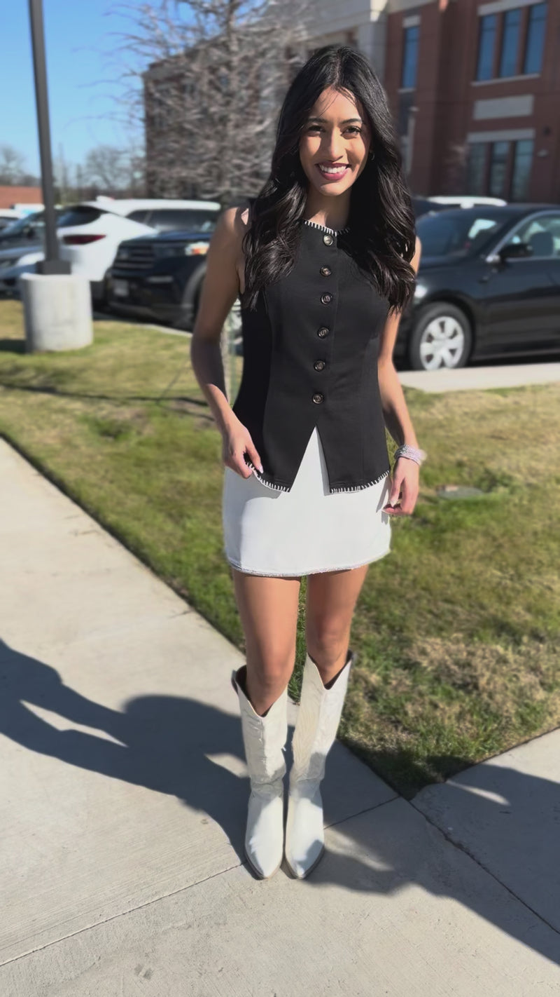 Woman wearing a black sleeveless vest over a white dress outside.