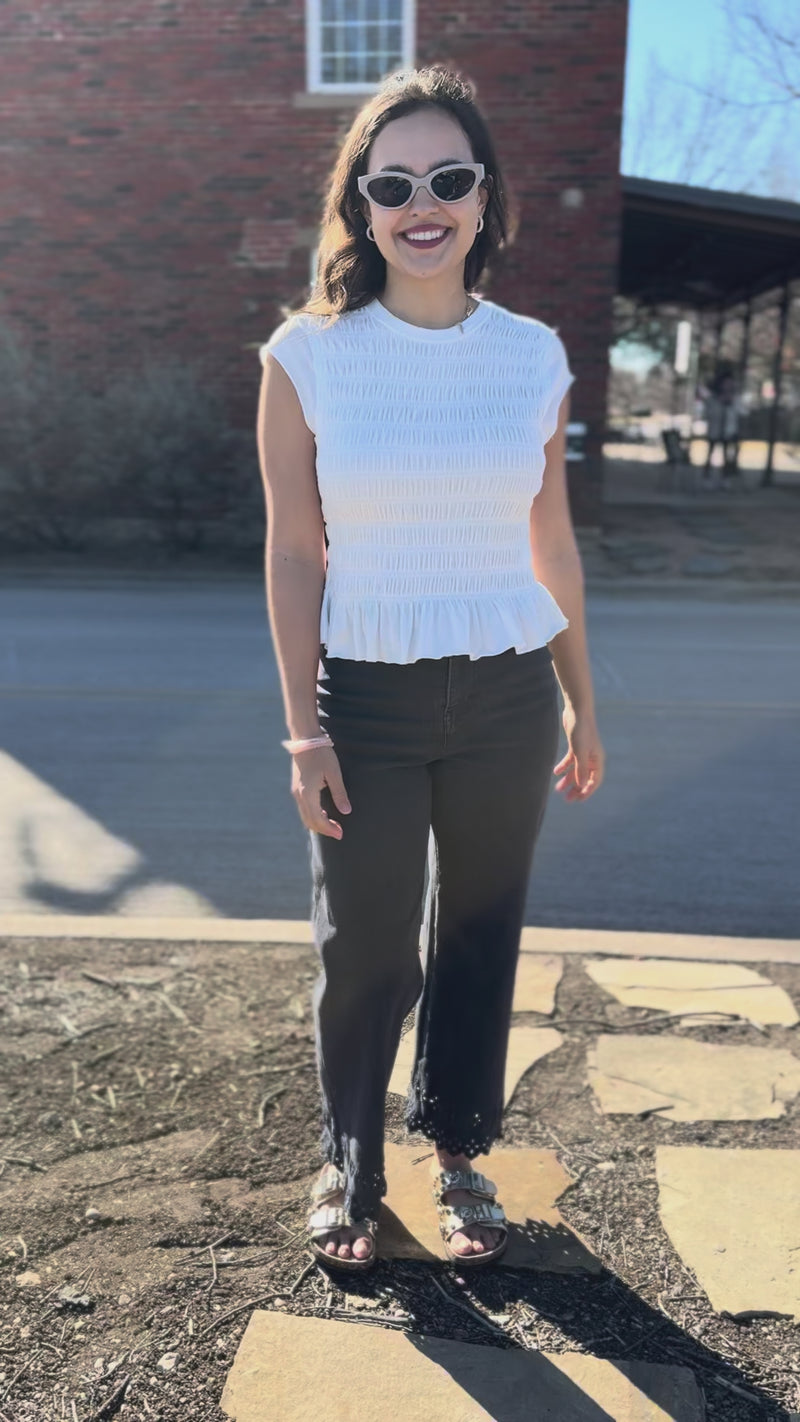 Woman wearing a white peplum top and dark pants outdoors.