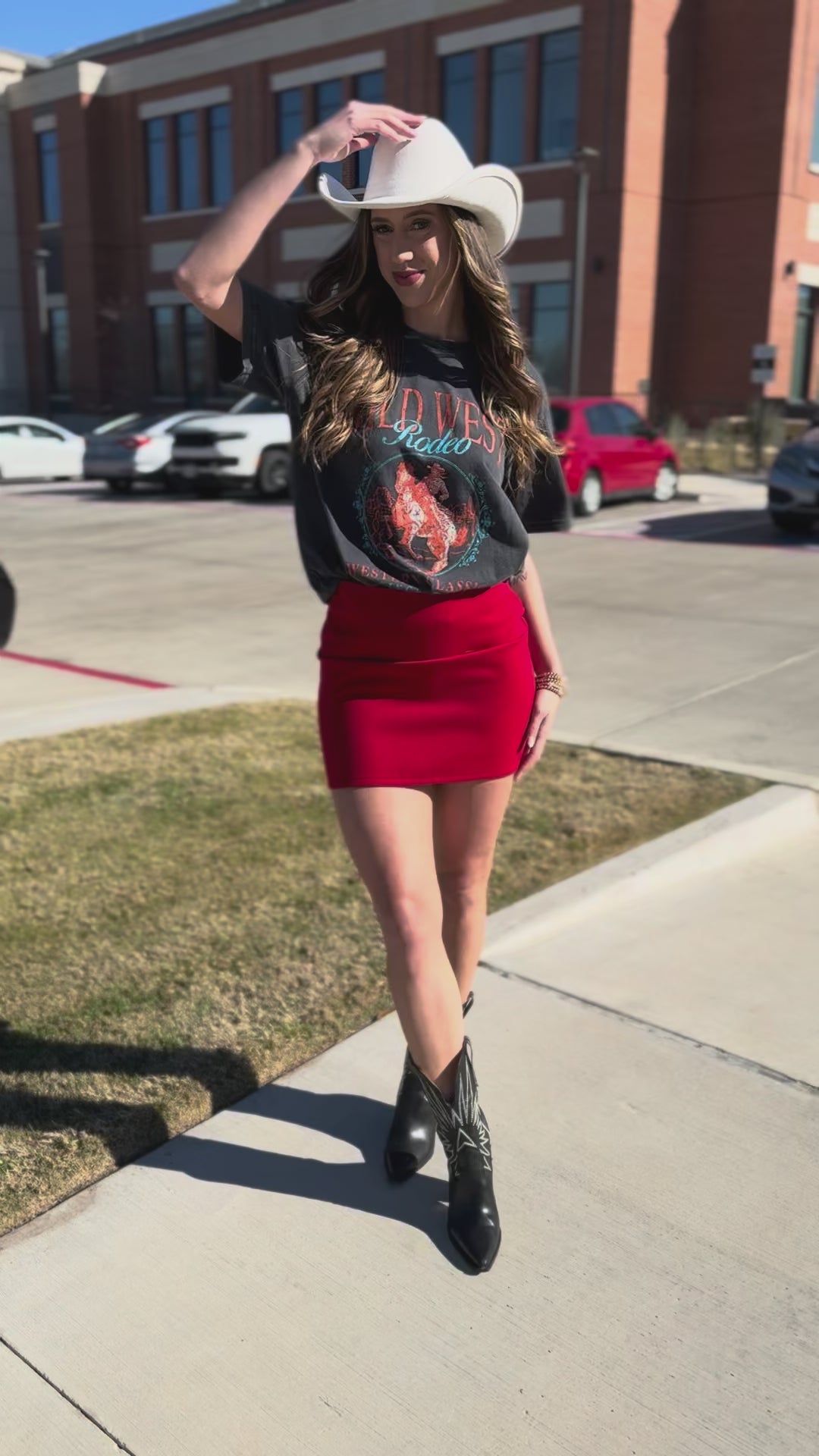 Woman wearing a graphic t-shirt, red skirt, and cowboy boots on a street.