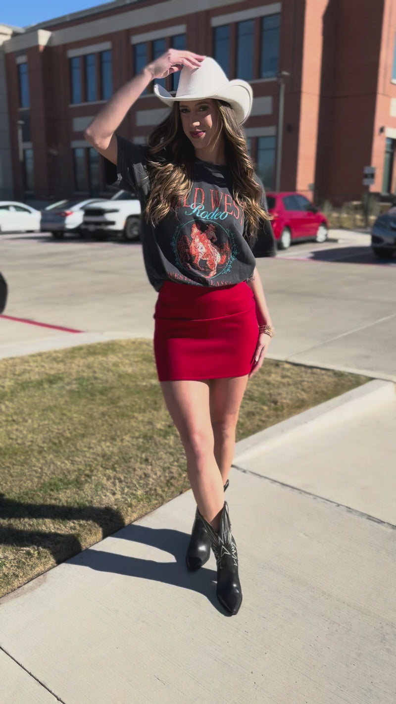 Woman wearing a graphic t-shirt, red skirt, and cowboy boots on a street.