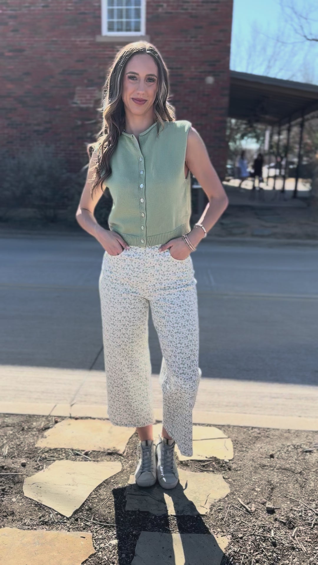 Woman wearing a green top and white patterned pants standing outside.