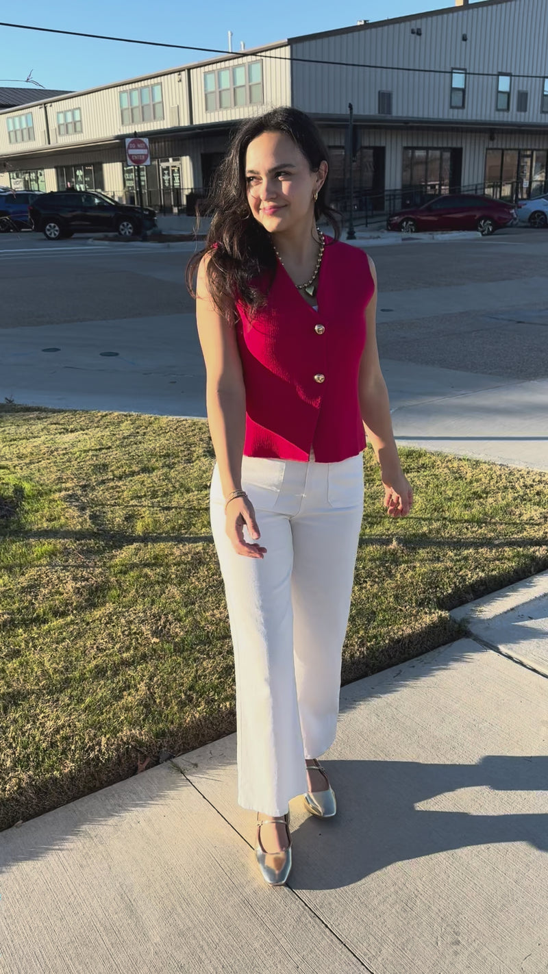 Woman wearing a red sleeveless top and white pants outdoors.