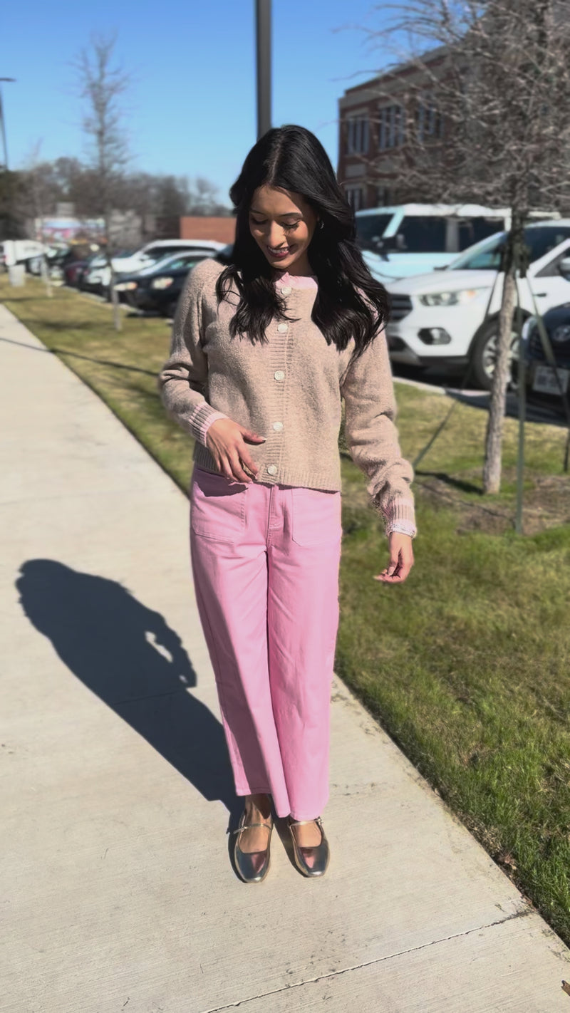 Woman wearing a beige cardigan and pink pants standing outdoors.