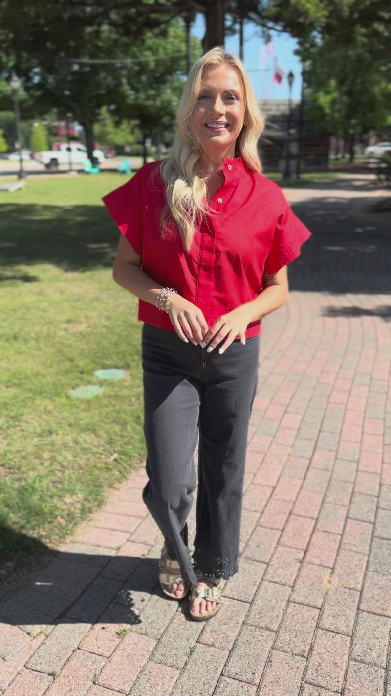 Blonde model wearing a red top with black denim pants standing outside.