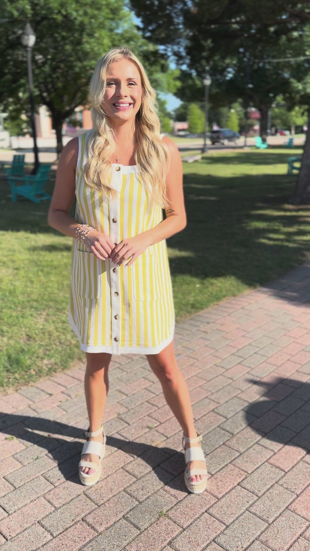 Woman in a yellow and white striped dress standing outside.