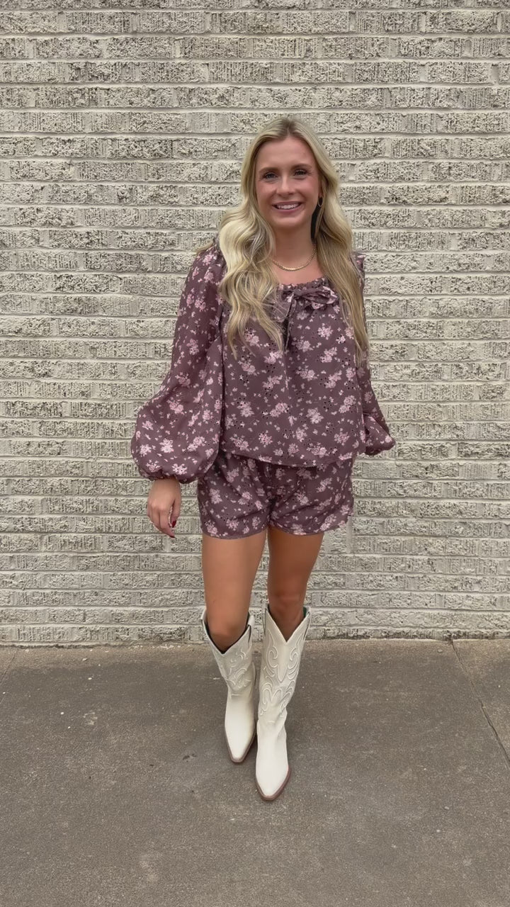 Blonde model wearing a brown floral eyelet set with white boots standing outside. Southern House Clothing