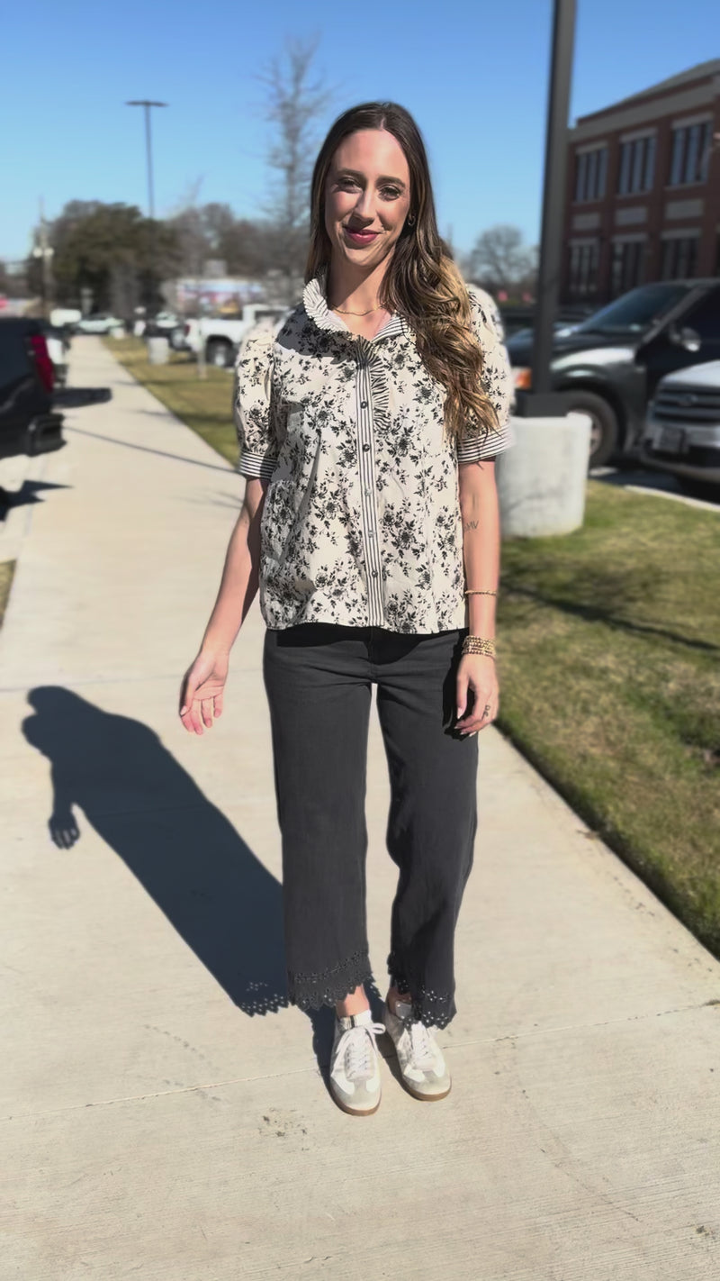 Woman wearing a floral blouse and dark pants outdoors.
