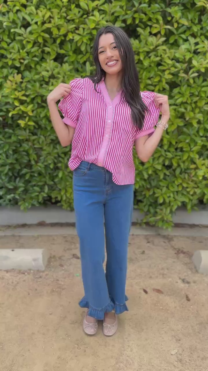 Woman wearing a pink striped shirt and blue jeans standing outdoors.
