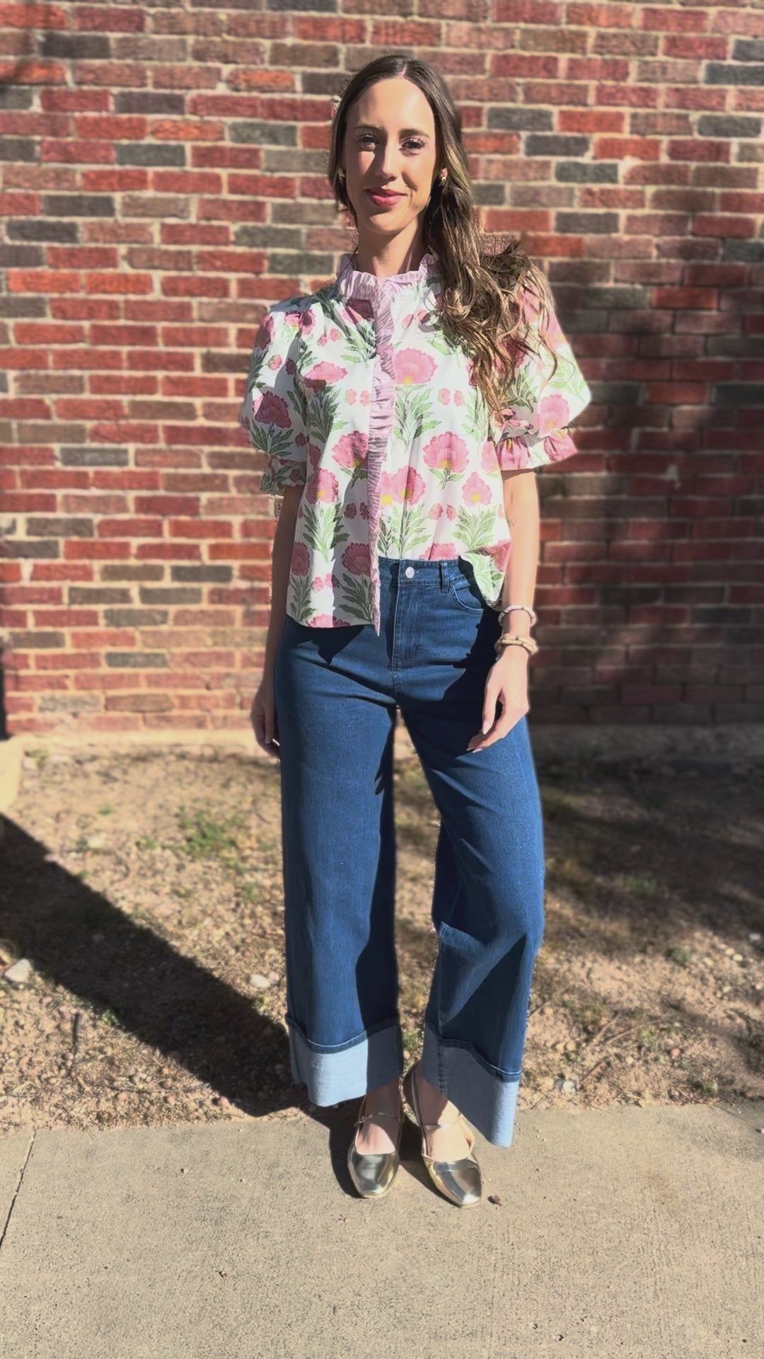 Woman wearing a floral blouse with pink flowers and green leaves, standing outside.