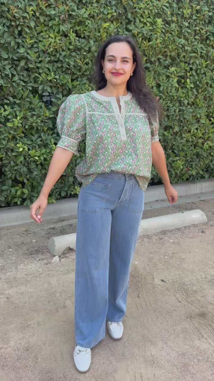 Brunette model in an olive top and jeans in an outdoor setting. Southern House Clothing