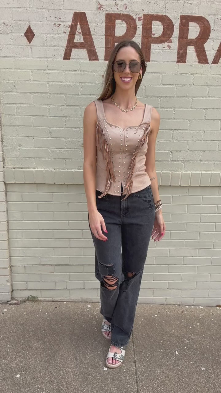 Blonde model wearing Laredo Luxe Studded Fringe Top in Camel featuring silver-tone studs, western fringe, sweetheart neckline, and wide straps, styled with black denim standing outside. Southern House Clothing