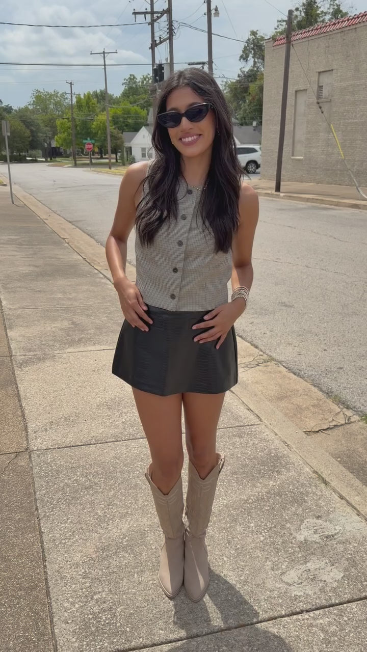 Brunette model wearing Westlake Check Button Vest in taupe and black micro-check pattern, featuring a round neckline, sleeveless design, and dark front buttons, paired with the Ranchero Faux Croc Skort in Black. Southern House Clothing