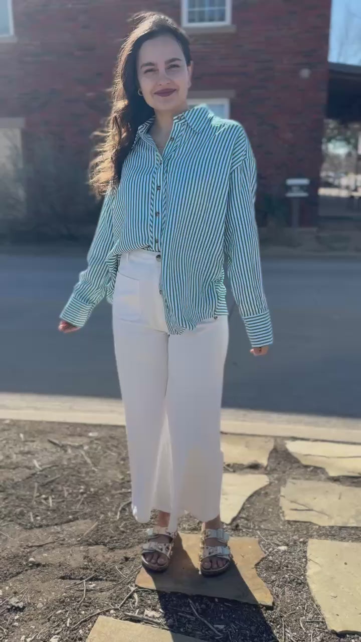 Woman wearing a green and white striped shirt and white pants on a sidewalk.