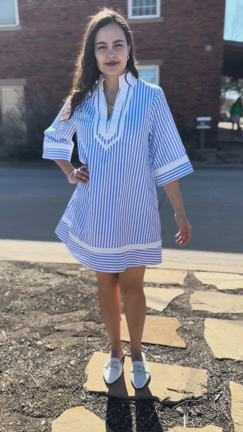 Woman wearing a blue and white striped dress with sneakers standing outside.