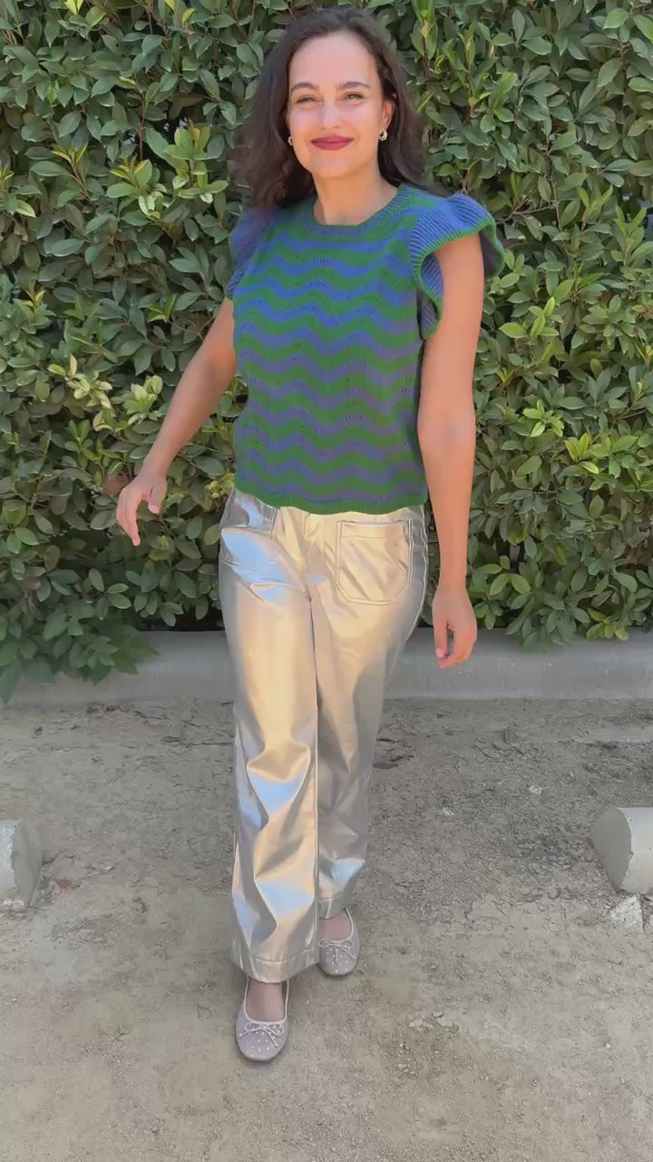 Brunette model wearing a blue and green sweater, silver pants, in an outdoor setting. Southern House Clothing