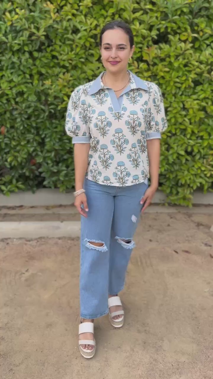 Woman wearing a floral blouse and jeans standing outside.