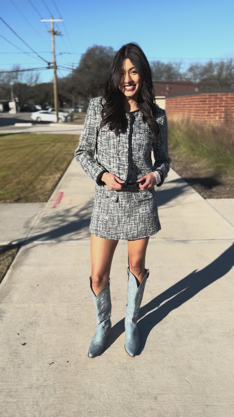 Woman in a tweed outfit with blue boots standing outdoors.