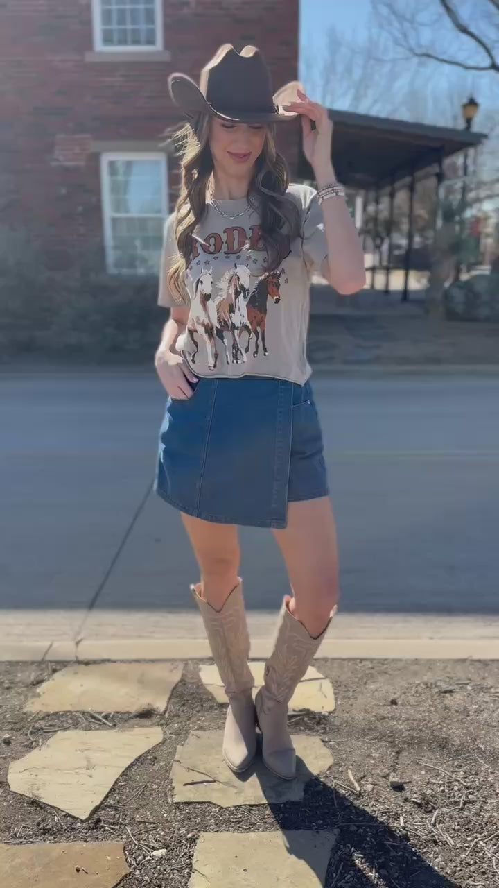 Woman wearing a 'Rodeo' graphic t-shirt with horses and a blue denim skirt.