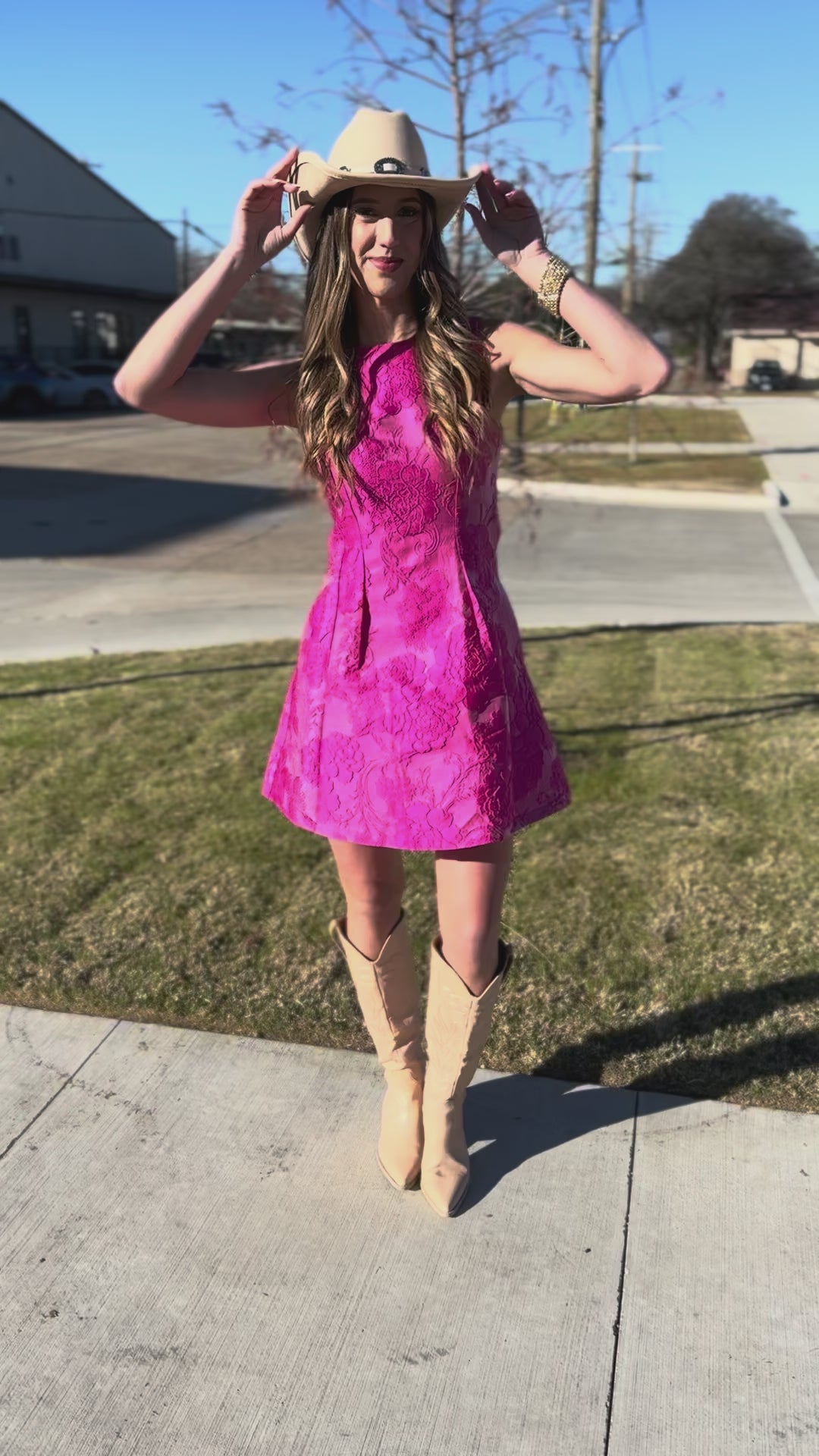 Woman in a pink dress and beige boots standing outside.