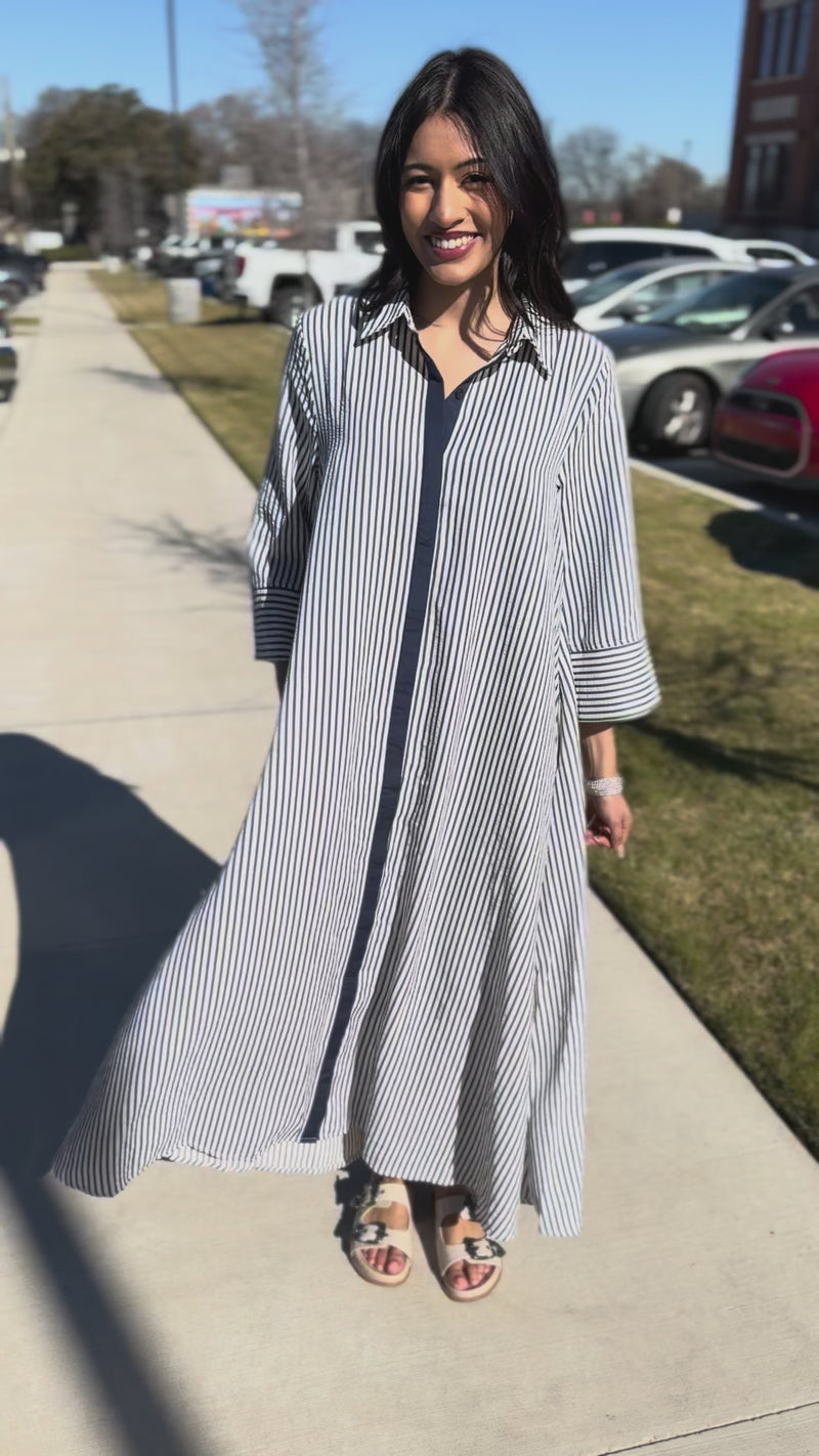Woman wearing a long, light-colored striped dress outside.