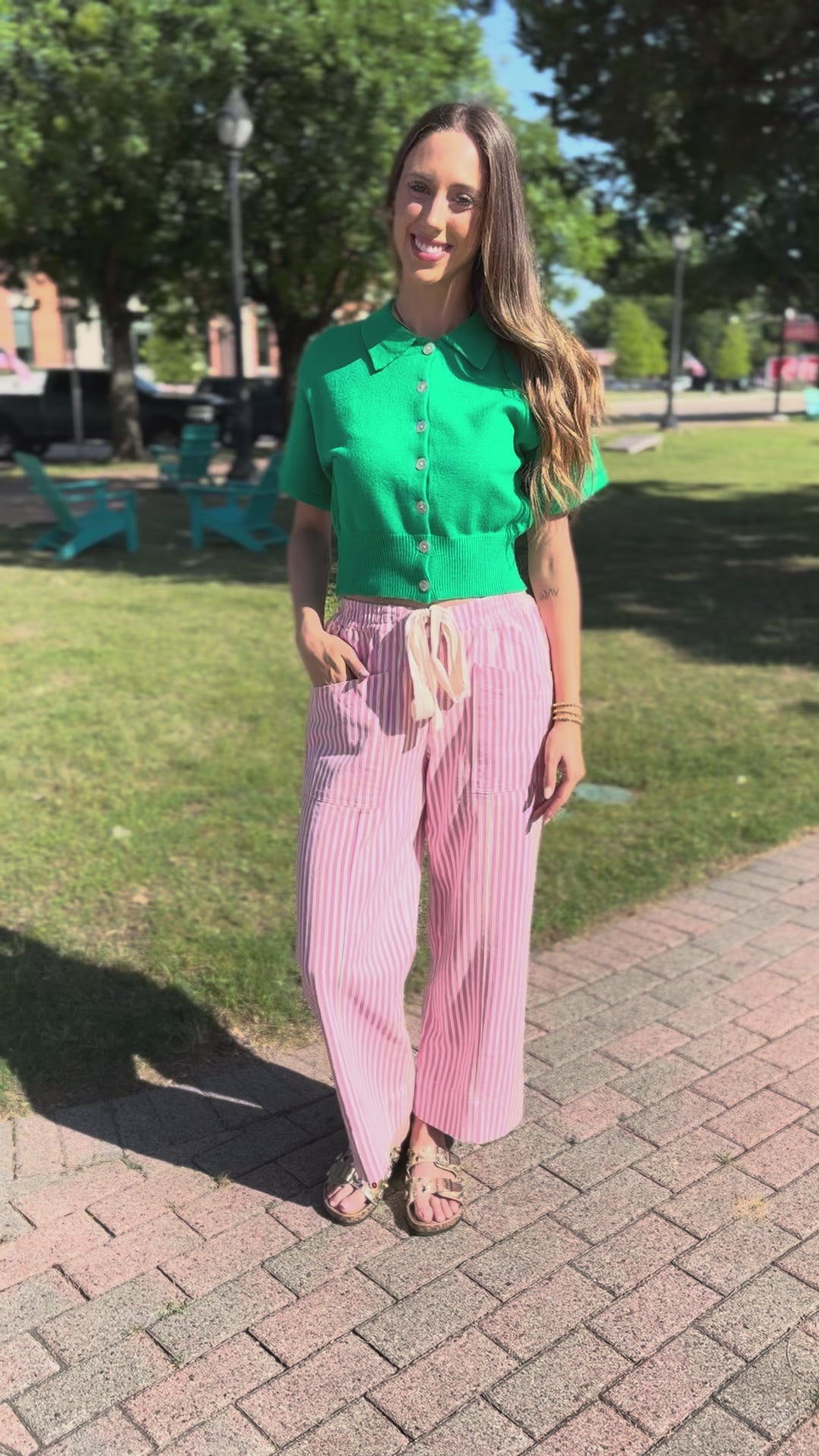 Woman wearing a green top and pink striped pants outdoors.